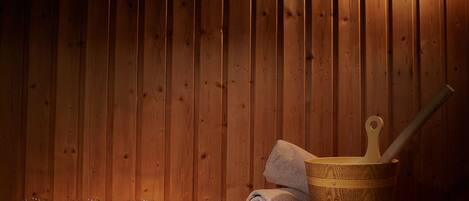 A wooden sauna with three lit candles, a rolled towel, and a wooden bucket with a ladle.