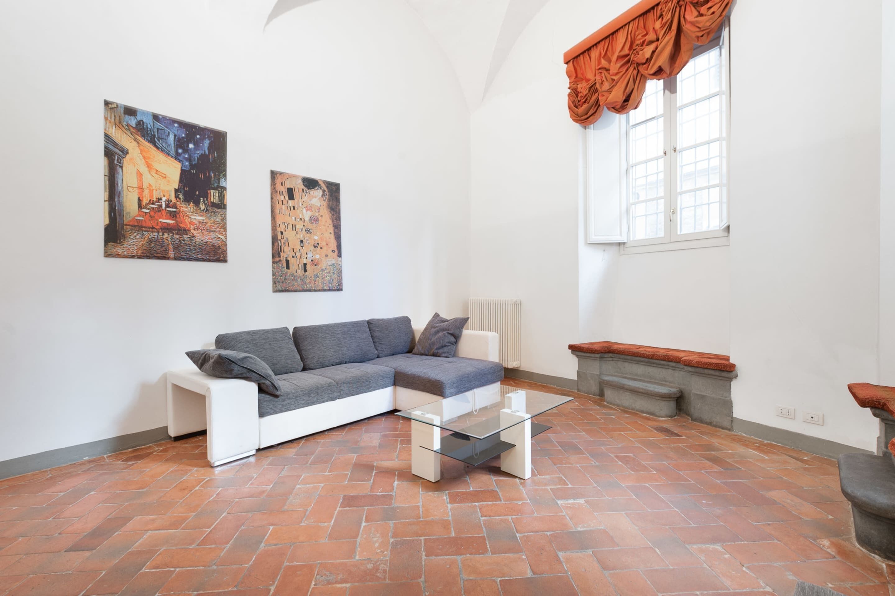 A modern living room with a sectional sofa, a glass coffee table, and two paintings on the wall.