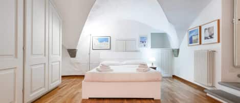 A bedroom with a large bed, wooden flooring, white walls, and a sloped ceiling.