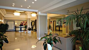 A modern hotel lobby with a reception desk, potted plants, and a staircase leading to other areas. - Hotel Delle Canne (Amantea)