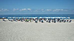 A beach with rows of blue and white umbrellas and lounge chairs facing the ocean. - Hotel Delle Canne (Amantea)