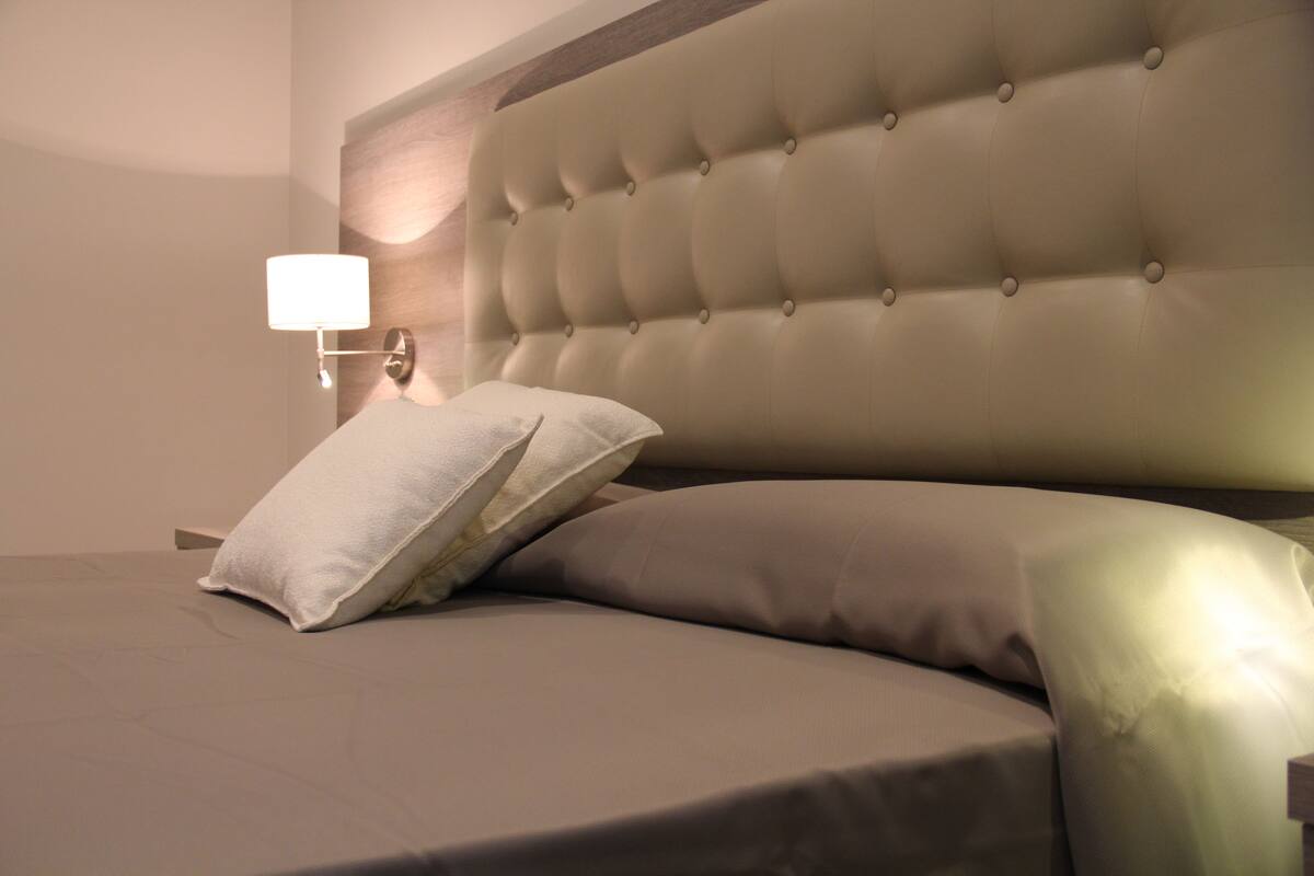 A neatly made bed with a tufted headboard, a bedside lamp, and two pillows.