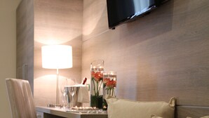 A modern hotel room with a sofa, a desk, a chair, a flat-screen TV mounted on the wall, and a lamp. - Hotel Delle Canne (Amantea)