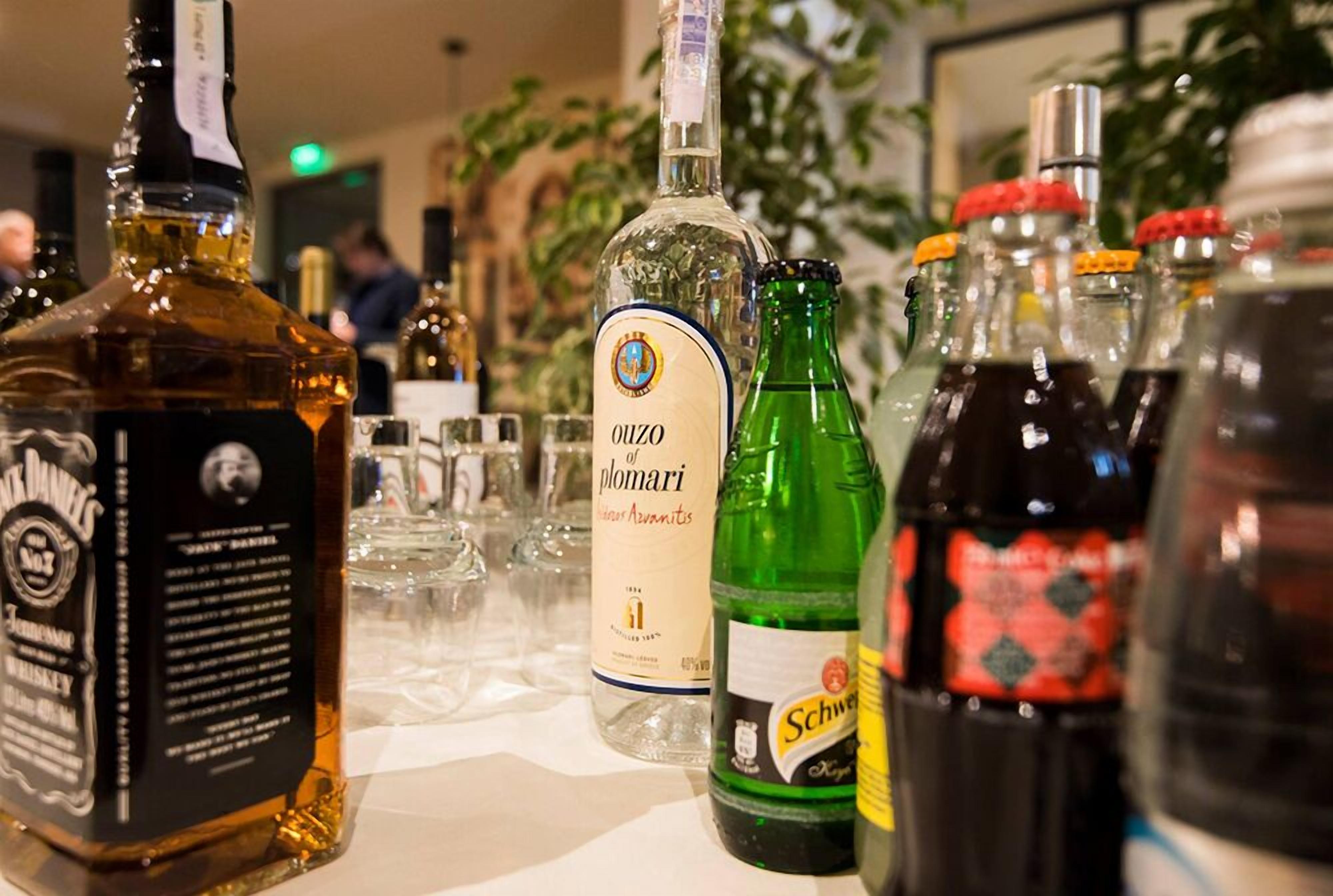 A variety of liquor bottles on a table, including brands like Jack Daniel's and Ouzo of Plomari.