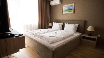 A hotel room with a bed, two bedside tables, a desk with a computer, and an air conditioning unit.