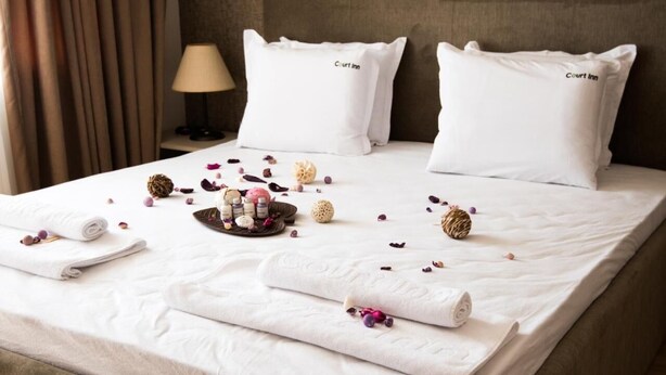 A neatly made bed with white linens, two pillows labeled "Court Inn," a tray with toiletries, and scattered rose petals. - Court Inn (Panagyurishte)