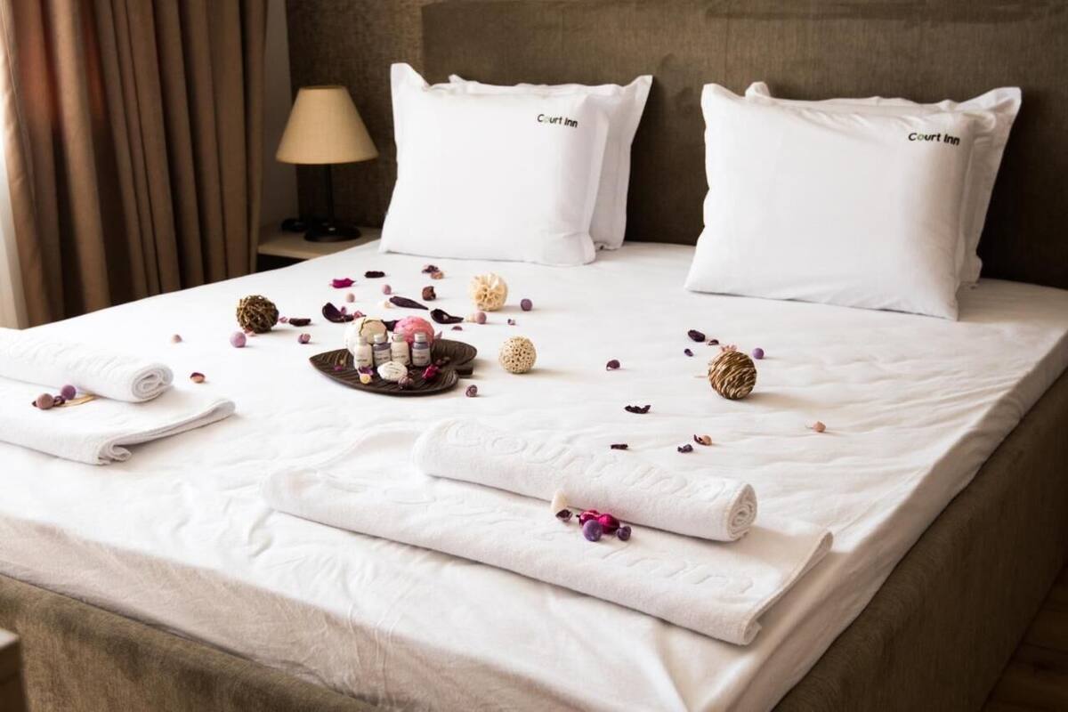 A neatly made bed with white linens, two pillows labeled "Court Inn," a tray with toiletries, and scattered rose petals.
