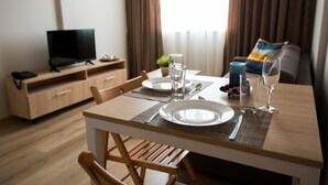 A hotel room with a dining table set for two, a television, and a sofa with a colorful pillow. - Court Inn (Panagyurishte)