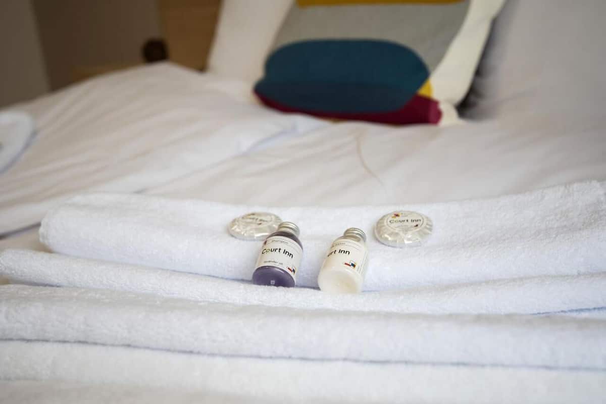 A neatly made bed with white towels and two bottles labeled "Court Inn" on a hotel room.