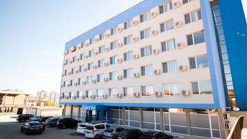 A multi-story hotel with a blue and white facade, air conditioning units, and a parking lot with several cars.