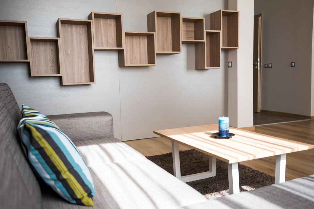 A modern living room with a sofa, a coffee table, and wooden shelves on the wall.