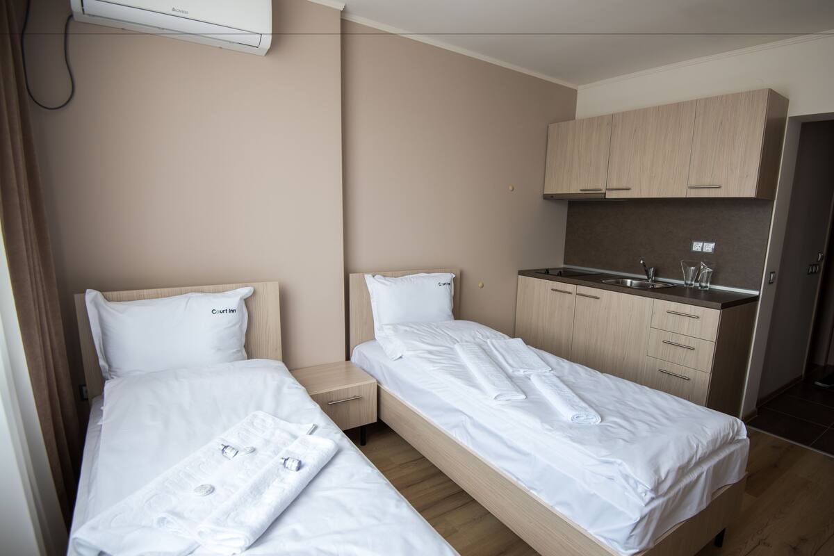A hotel room with two beds, a kitchenette, and a bathroom.