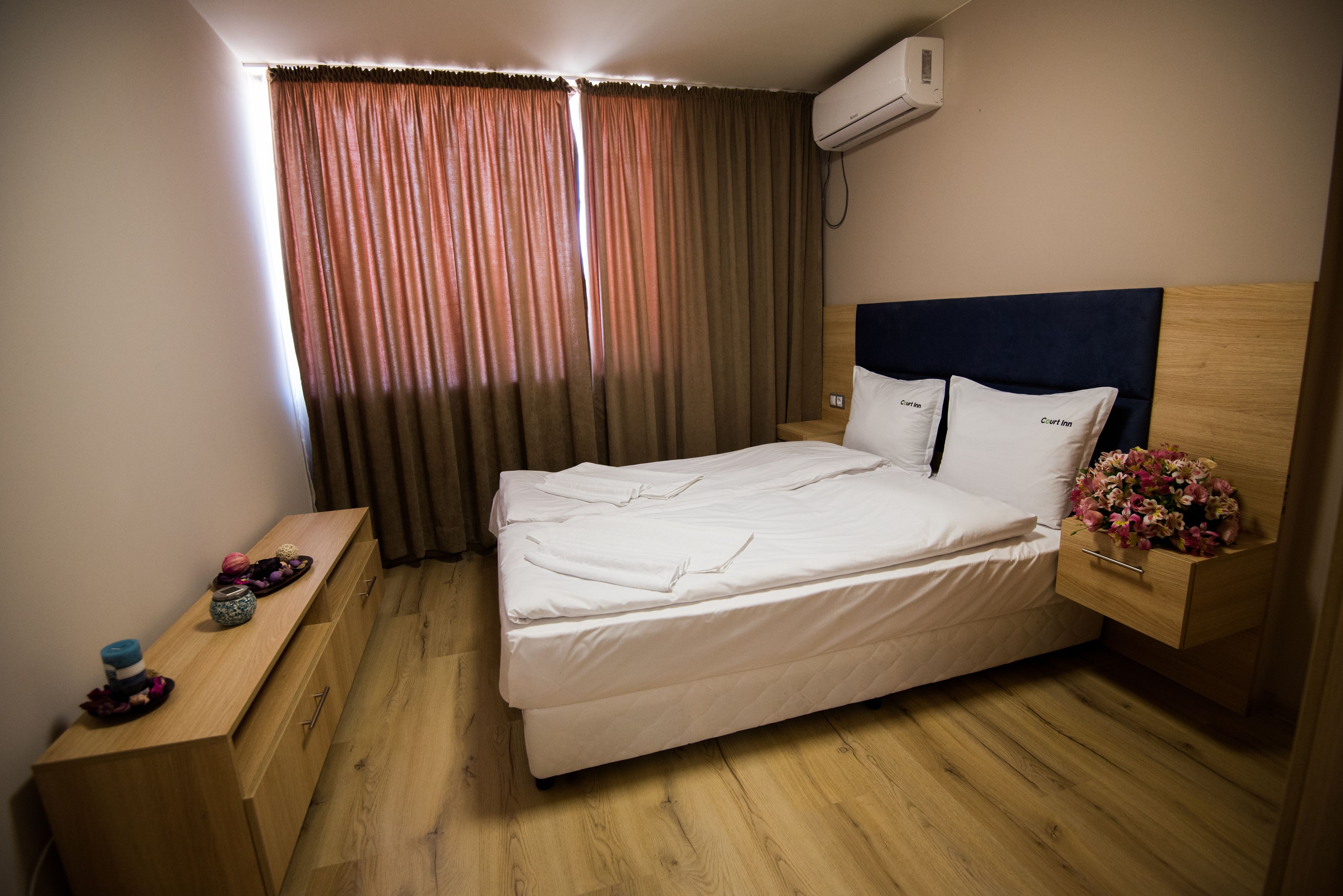 A hotel room with a bed, wooden nightstand, and a wall-mounted air conditioner.