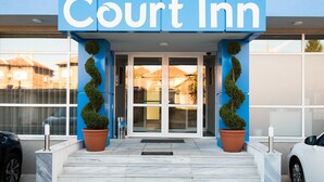 The exterior of a Court Inn hotel with a blue facade, double doors, and potted plants. - Court Inn (Panagyurishte)