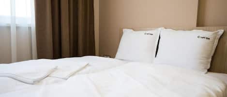 A hotel room with a neatly made bed, two pillows with the hotel name, and a window with curtains.