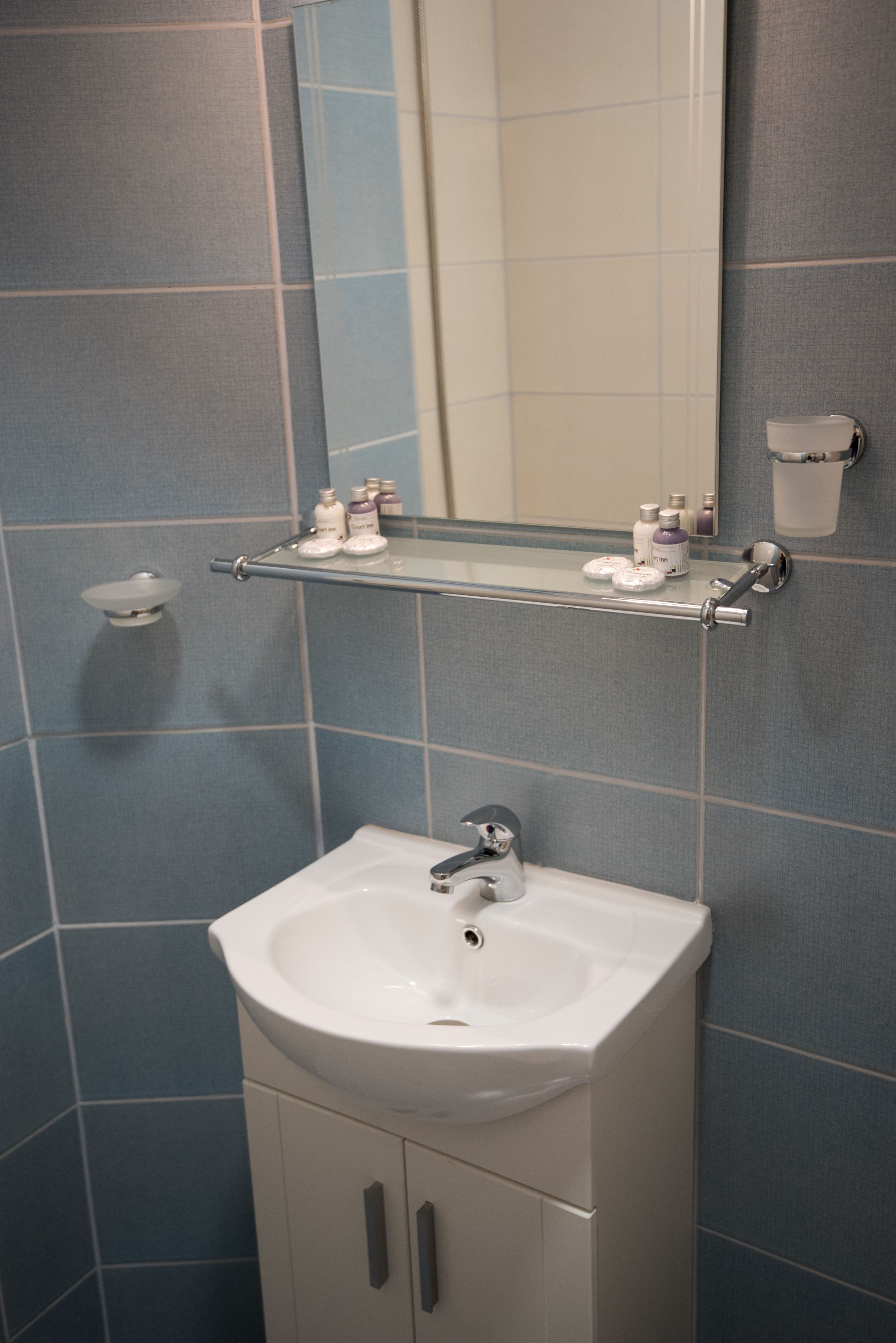 A bathroom with a white sink, a mirror, and a shelf with toiletries.