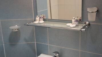 A bathroom with a white sink, a mirror, and a shelf with toiletries.