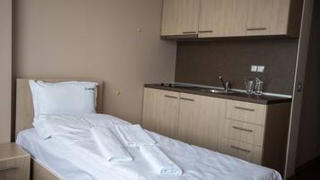 Hotelkamer met een bed, een klein nachtkastje, een ingebouwde kitchenette met een spoelbak en kastjes, en een raam.