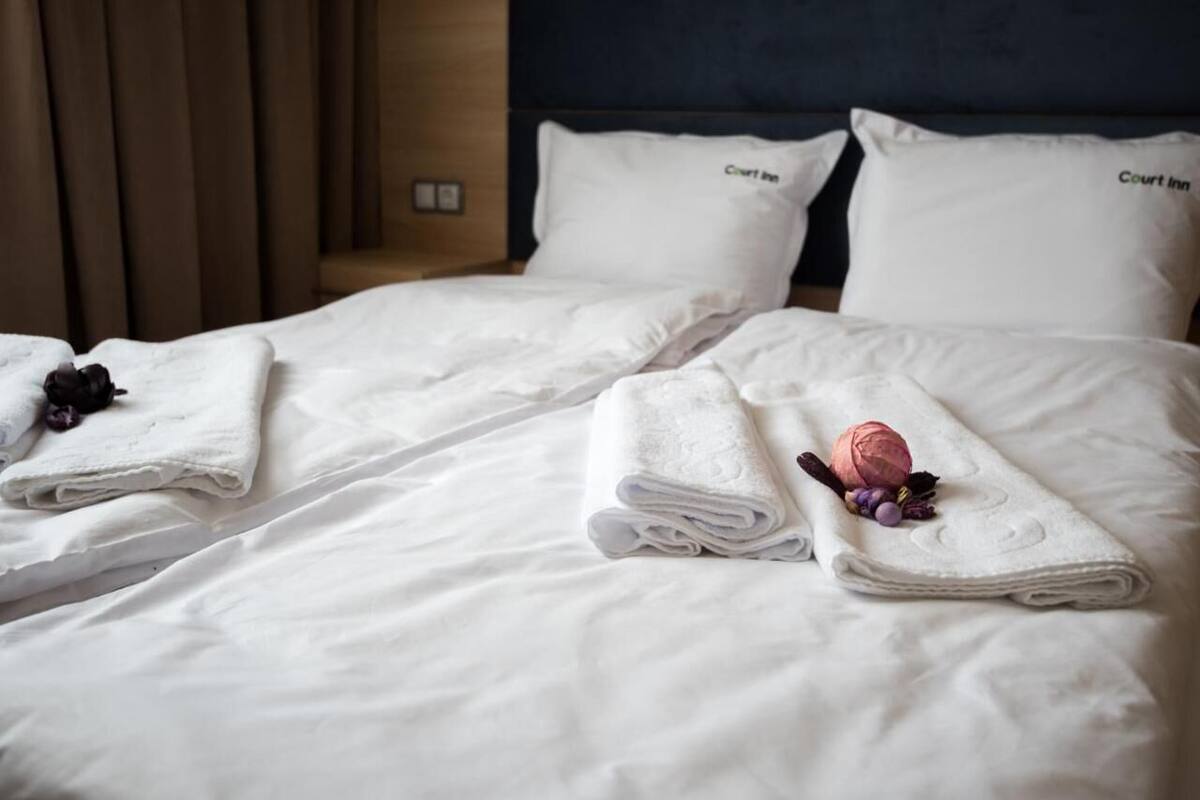A hotel room with two beds, each with a neatly folded white towel and a pink flower.