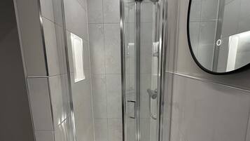 Un bagno moderno con cabina doccia in vetro, un lavandino bianco e uno specchio rotondo.