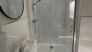 A modern bathroom with a glass-enclosed shower, a round mirror, and a white sink. - Contractors Guest House (High Wycombe)