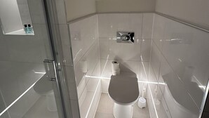A modern bathroom with a glass shower enclosure, a toilet, and a small shelf with toiletries. - Contractors Guest House (High Wycombe)