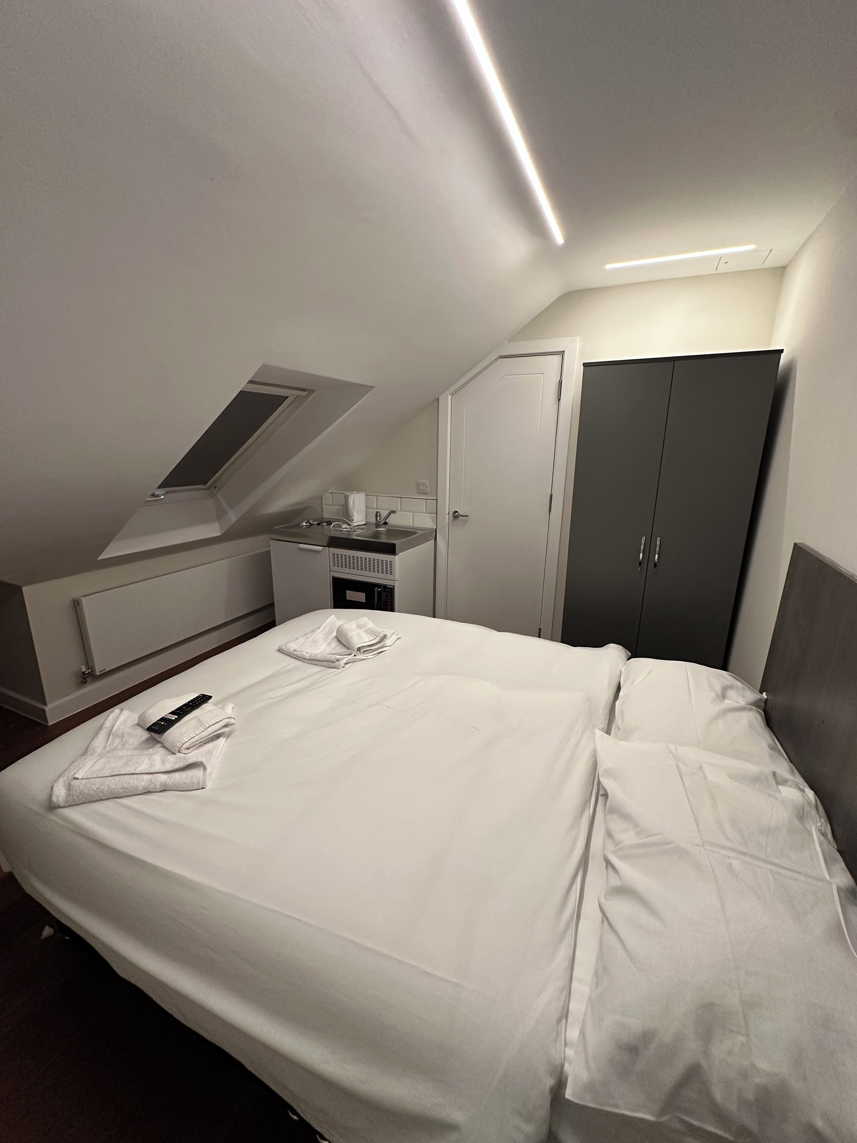 Et hotelværelse med seng, skrivebord, garderobeskab og skydeluger.