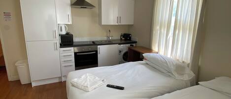 Una habitación de hotel compacta con dos camas, kitchenette y baño.