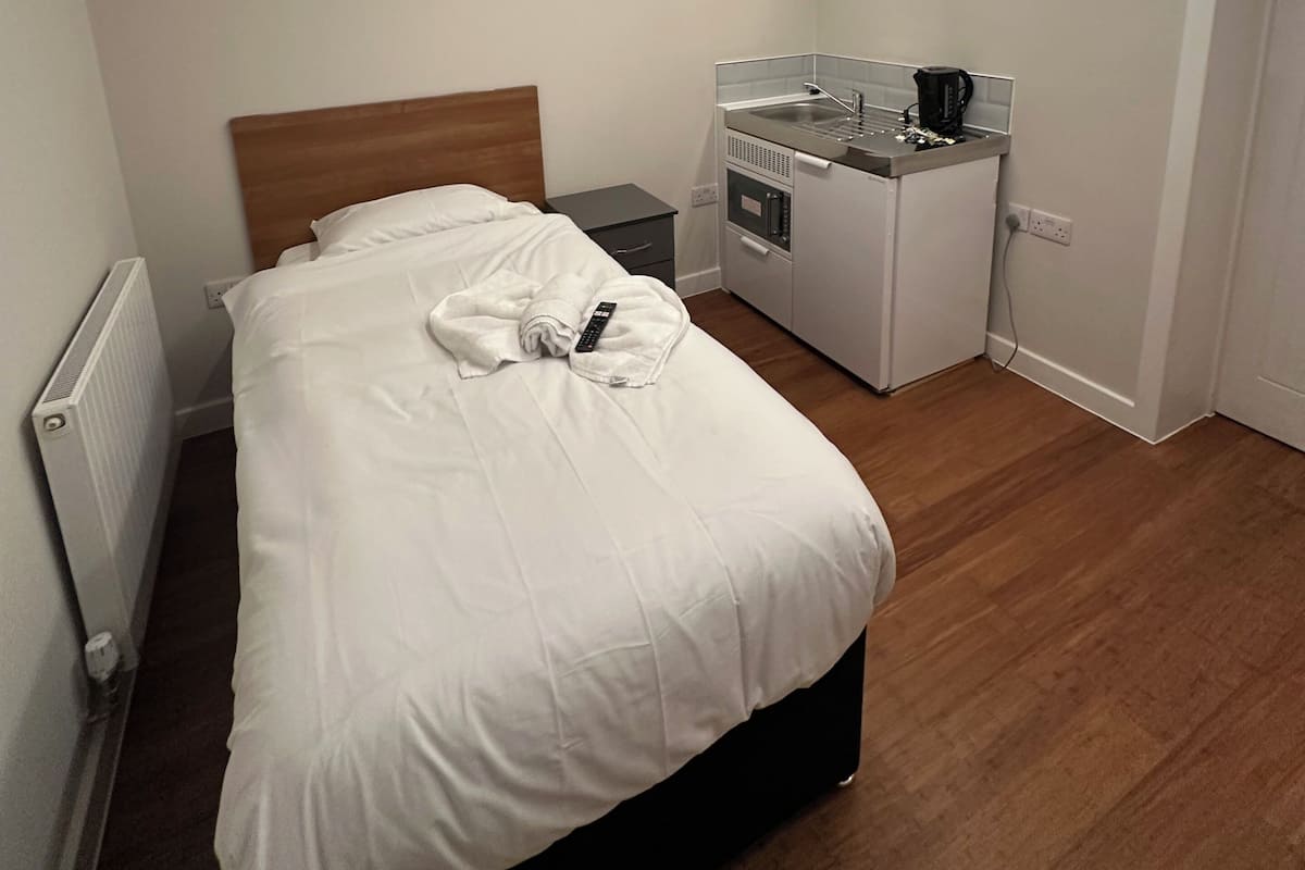 Una camera d'albergo con un letto, un comodino, un angolo cottura e un termosifone.