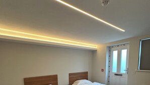 A hotel room with two beds, a nightstand, a radiator, and a window with curtains. - Contractors Guest House (High Wycombe)