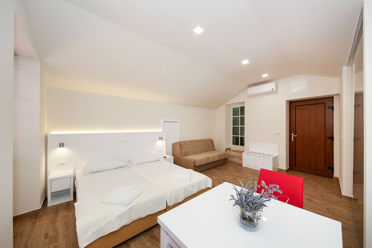 A modern hotel room with two beds, a sofa, a small table, and a red chair.