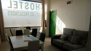 A hotel room with a dining table, chairs, a sofa, and a projection screen displaying the hotel's name.