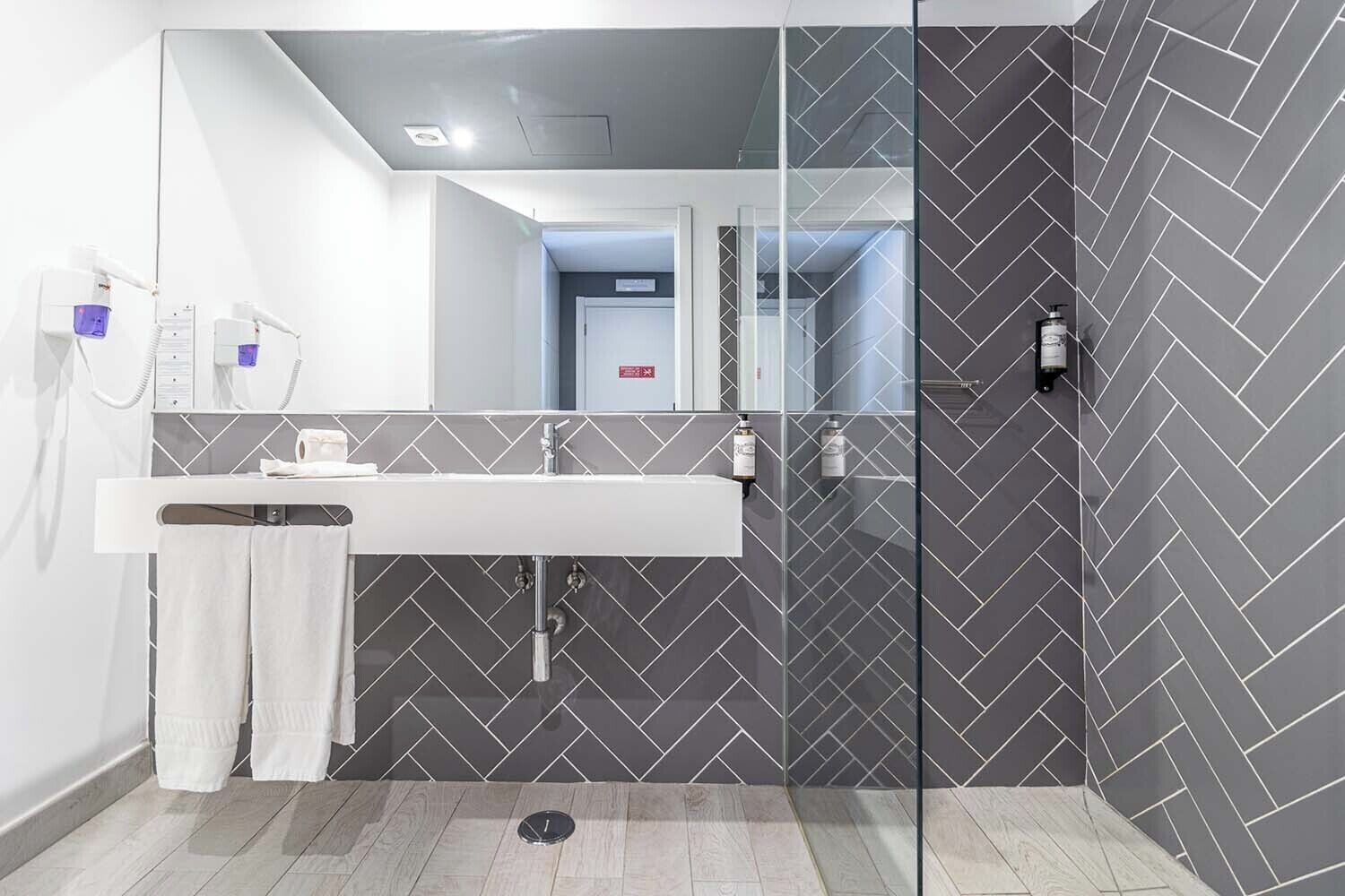 A modern bathroom with a glass shower enclosure, a white sink, and a mirror.