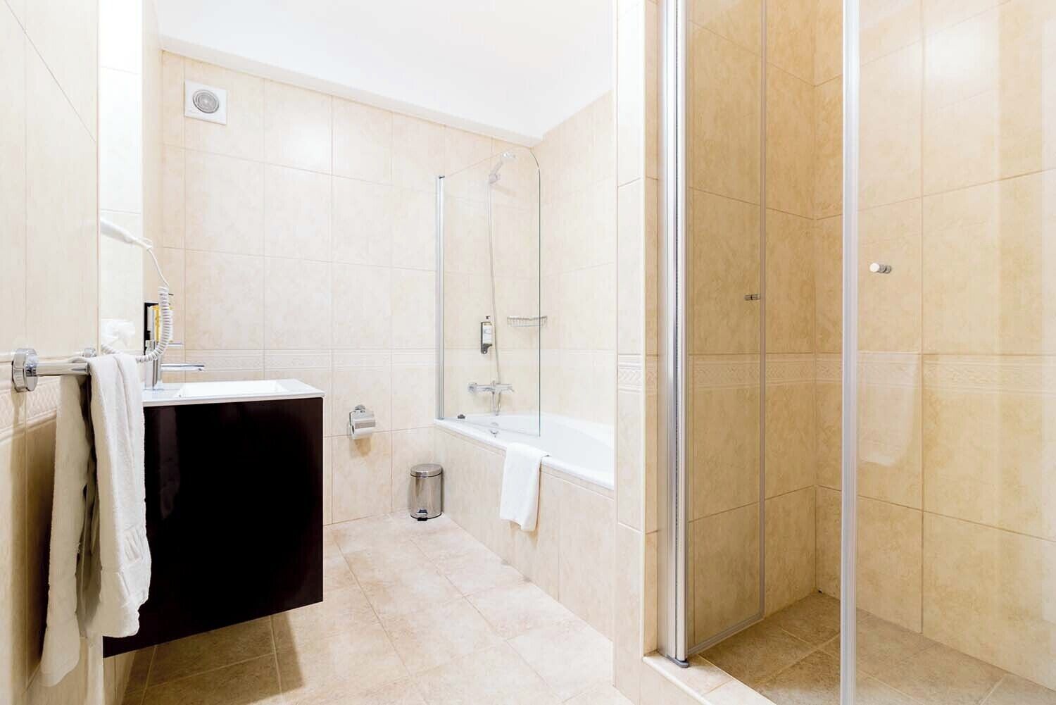 Un baño moderno con ducha envuelta en vidrio, tocador negro y bañera blanca.