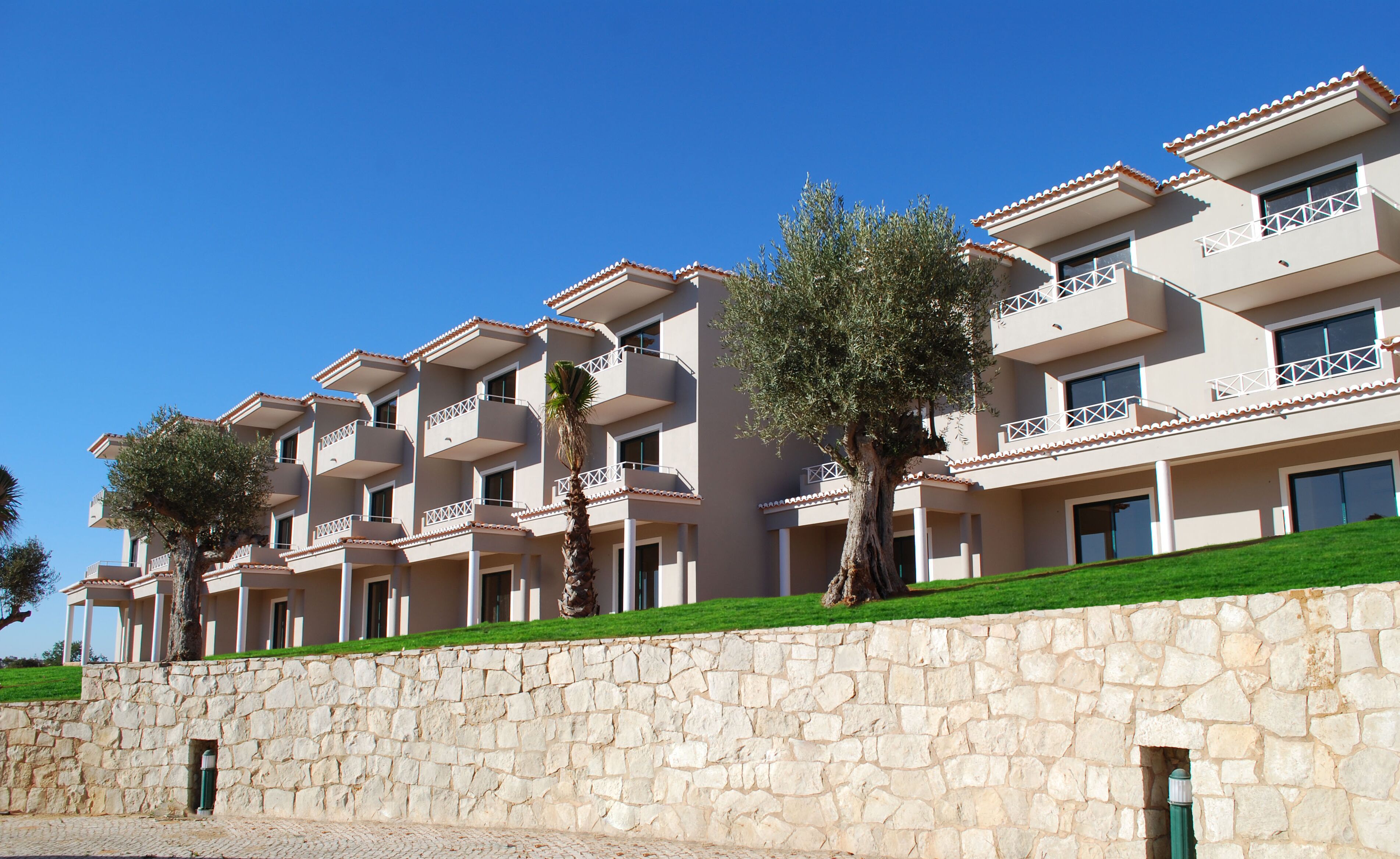 A multi-story hotel with balconies, stone walls, and green lawns.