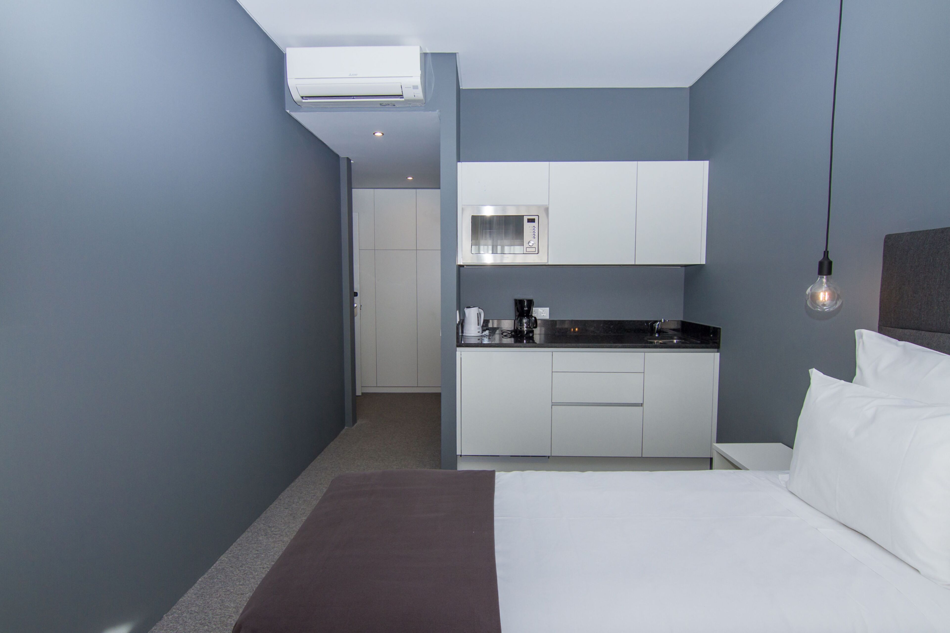 Una habitación de hotel moderna con kitchenette, una cama y una lámpara colgante.