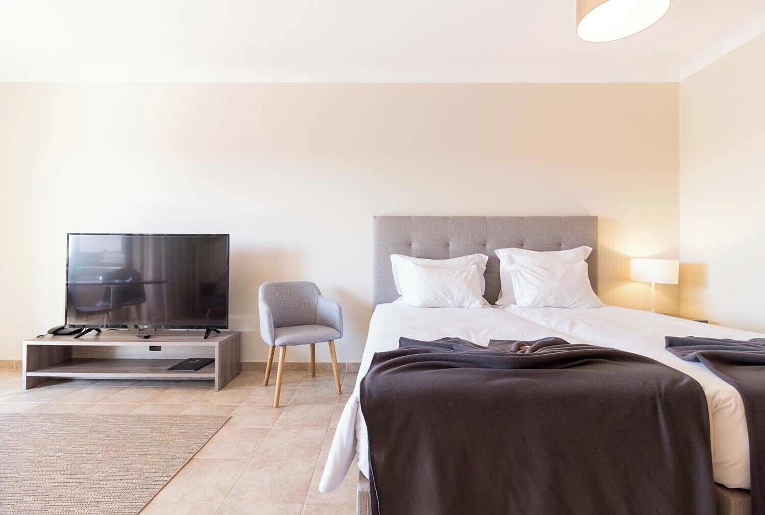 Una habitación de hotel con cama, televisión, sillón y mesita de noche.