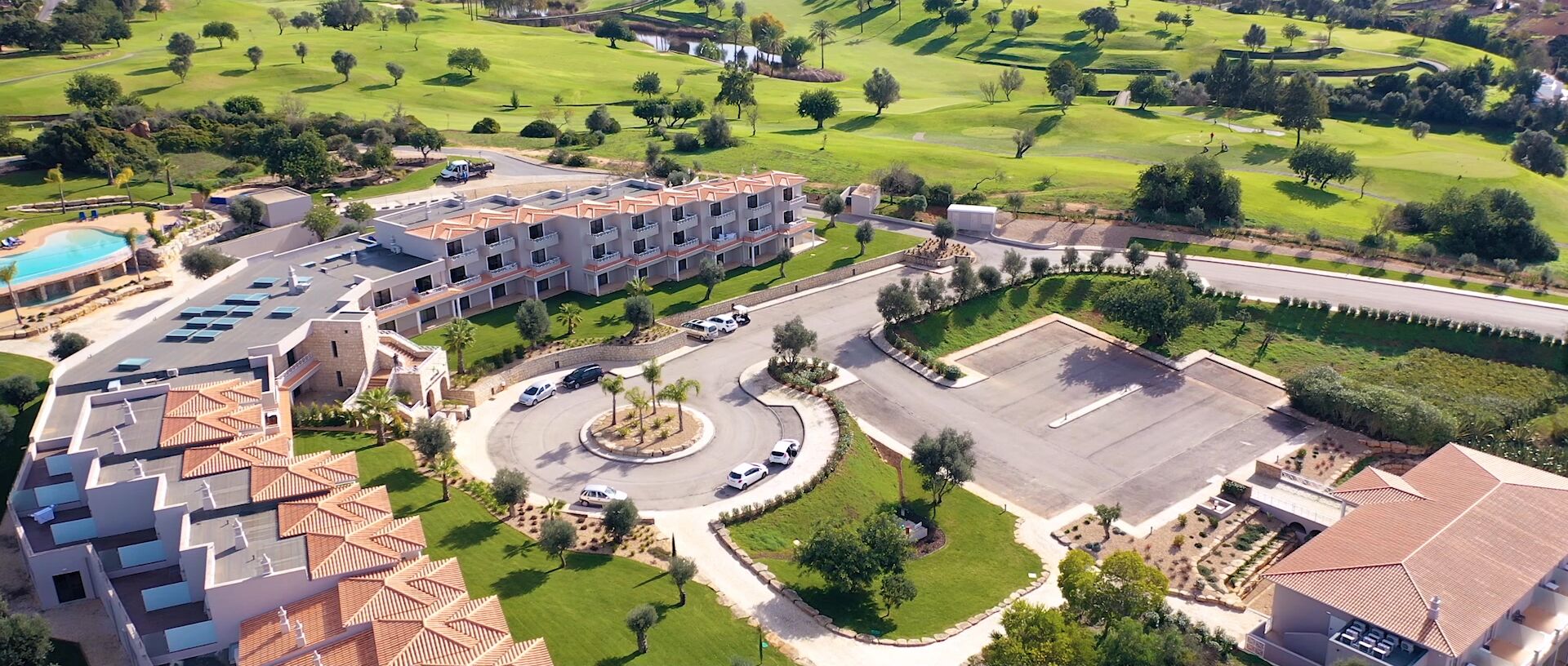 An aerial view of a hotel with multiple floors, a central courtyard, and a golf course in the background.