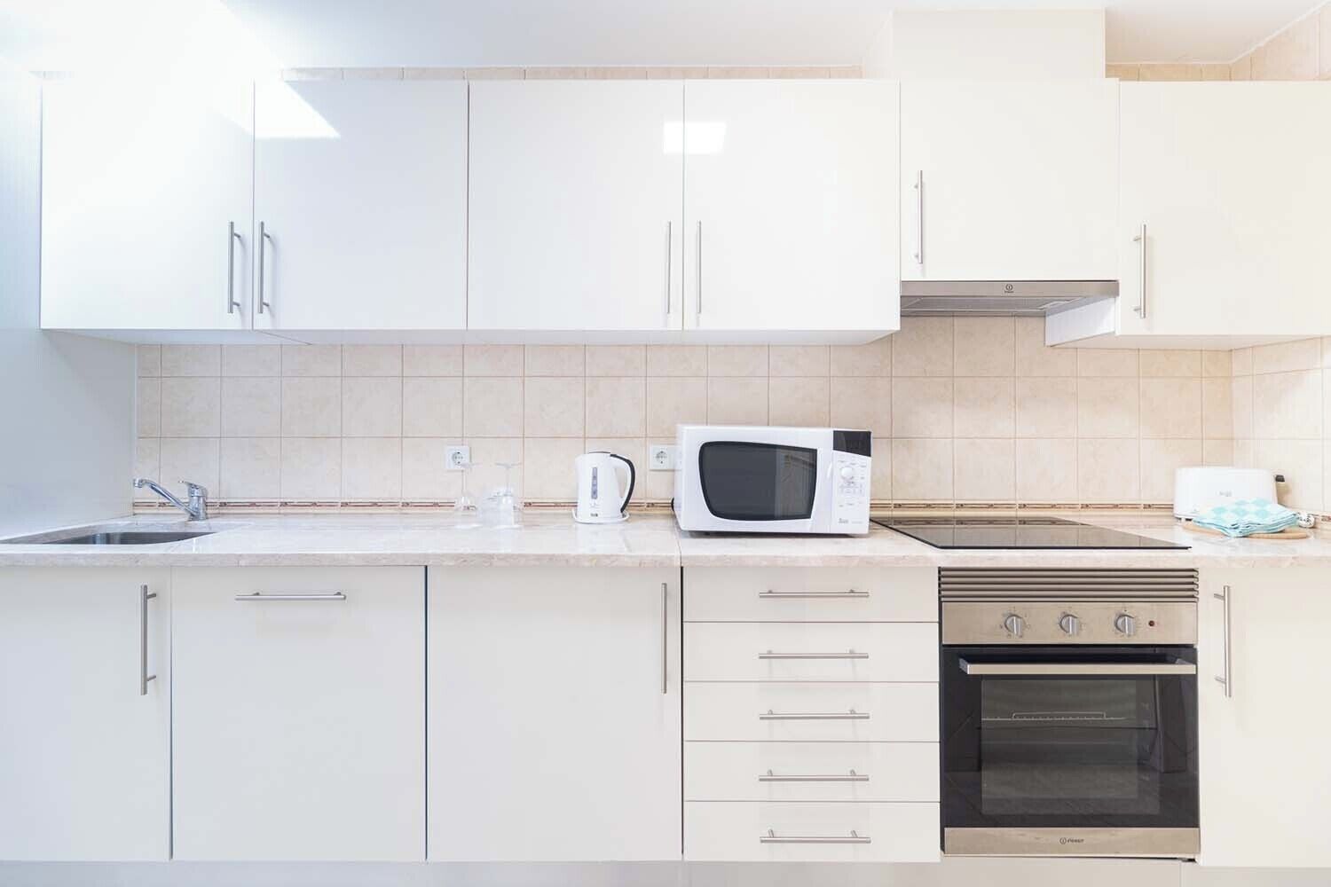 A modern kitchen with white cabinets, a microwave, a stove, and a sink.