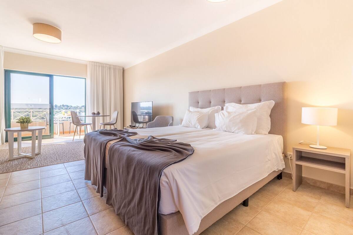 Une chambre d’hôtel avec un grand lit, une télévision, un bureau avec une chaise et un balcon avec vue.