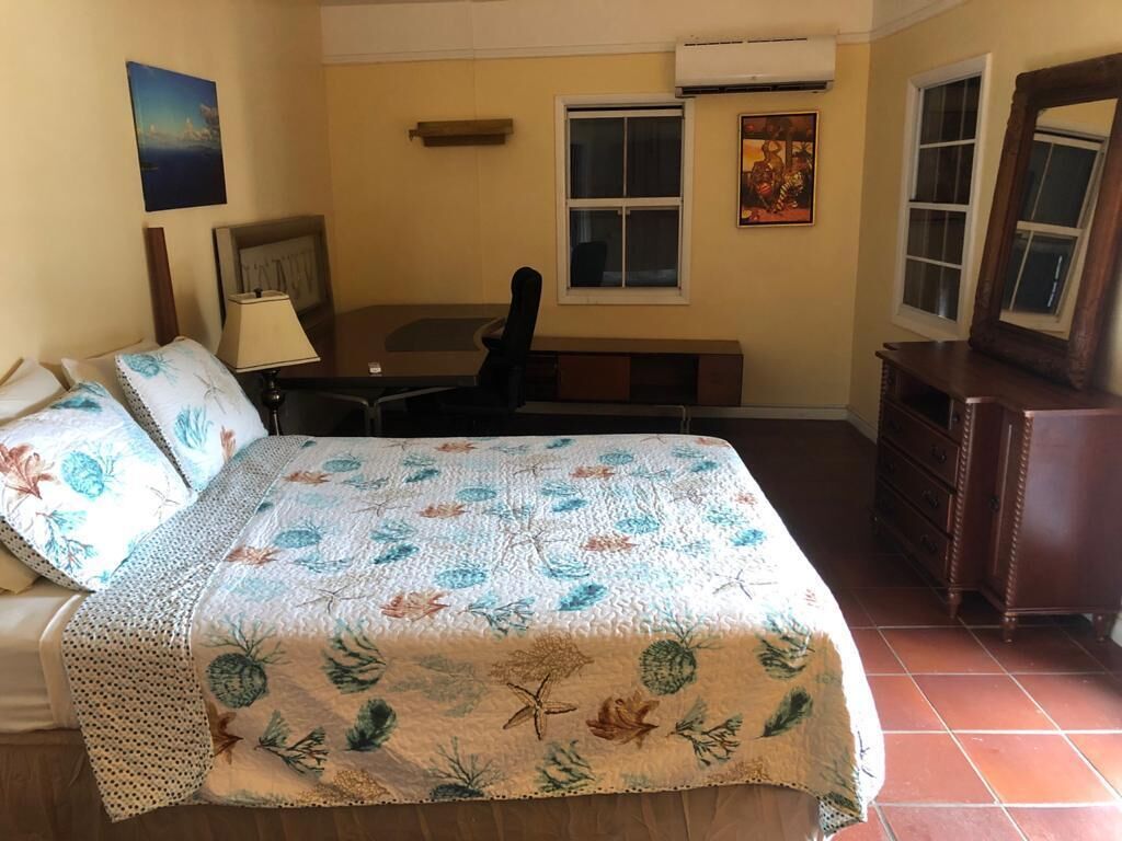 Une chambre à coucher comprenant un lit, un bureau, une chaise, une commode et deux fenêtres.