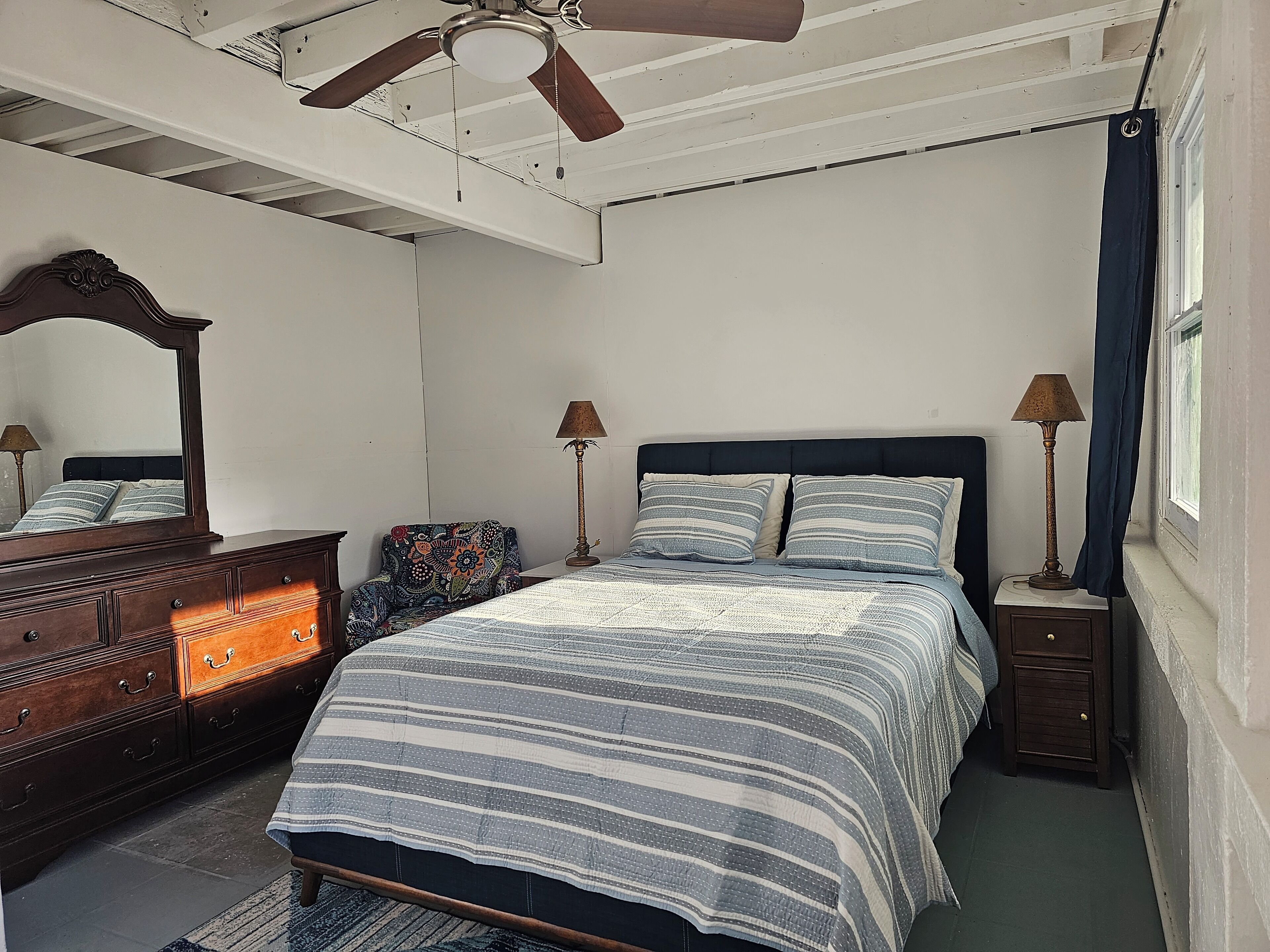 Un dormitorio con cama, cómoda, mesita de noche, lámpara y ventilador de techo.