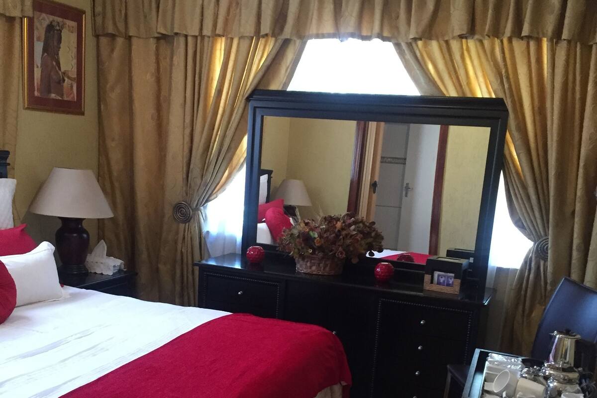 A hotel room with a large bed, a dresser, a mirror, and a chair.