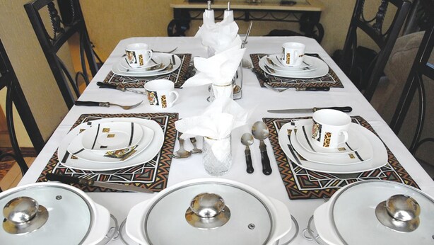 Una mesa de comedor dispuesta formalmente, con platos, fuentes y cubiertos blancos.