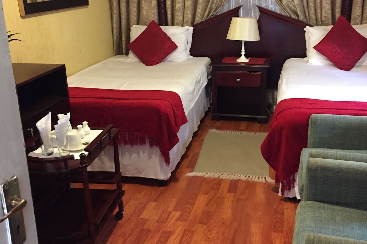 A hotel room with two beds, a desk, a chair, and a window with curtains.
