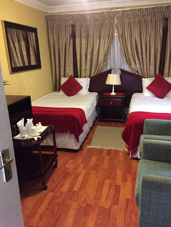 A hotel room with two beds, a desk, a chair, and a window with curtains. - Dithakong Bed & Breakfast (Soweto)