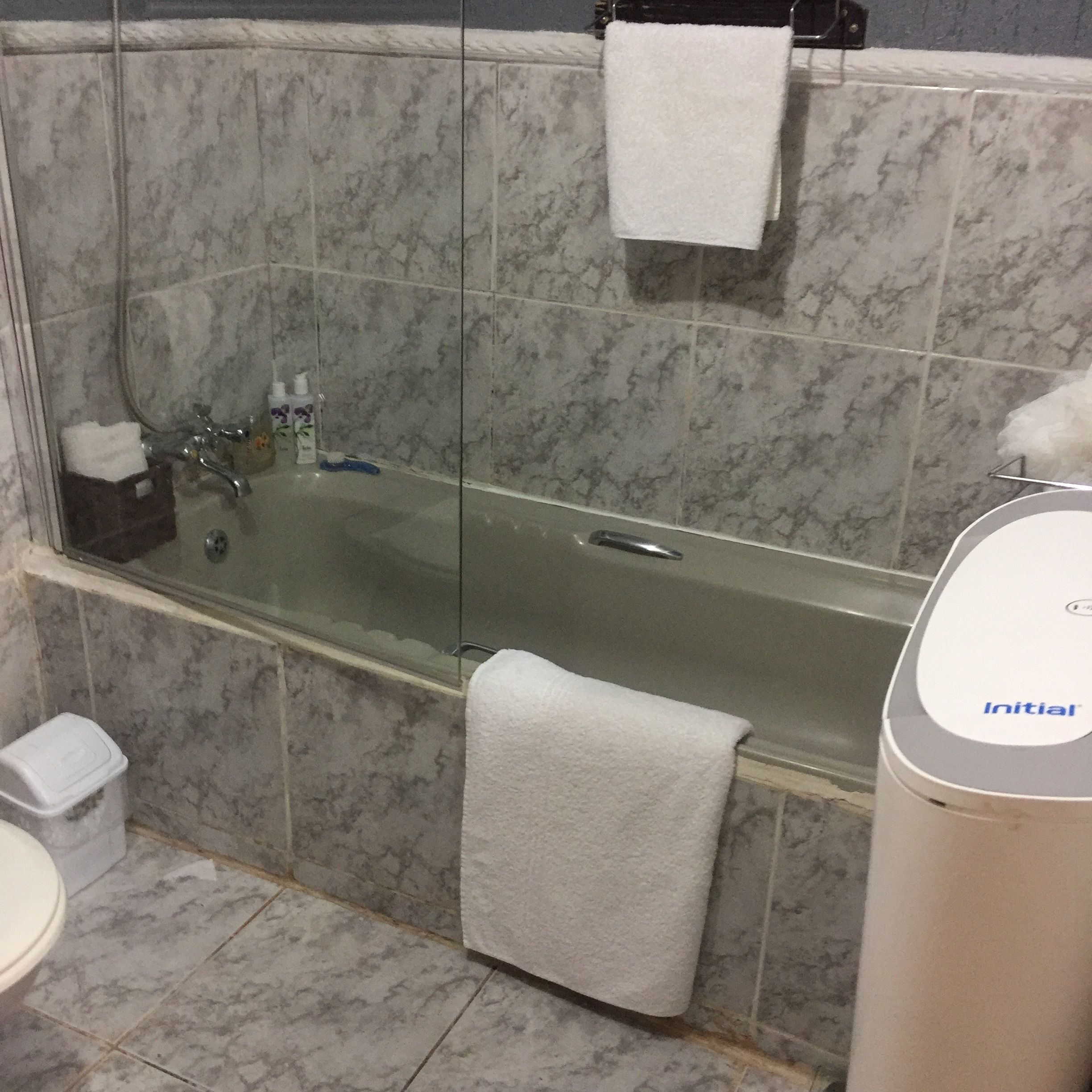 Un baño con bañera de hidromasaje con mampara de vidrio, una toalla blanca colgada en la pared y un inodoro.