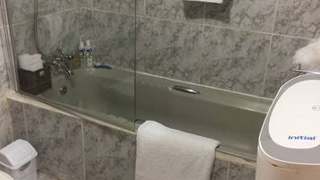 Un baño con bañera de hidromasaje con mampara de vidrio, una toalla blanca colgada en la pared y un inodoro.