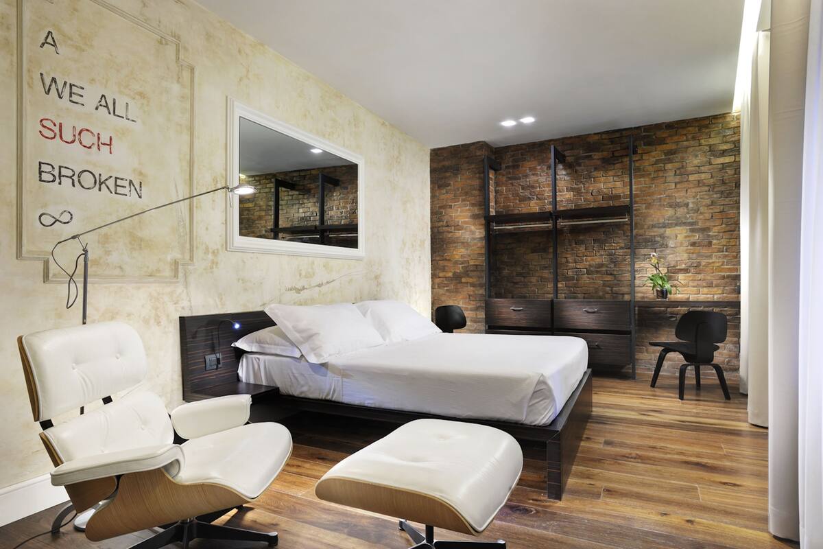 Un dormitorio moderno con una pared de ladrillo decorativa, una cama grande, una silla blanca y un escritorio con una planta.