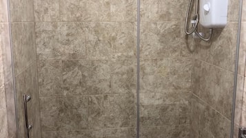 Una ducha a nivel con puerta de vidrio, azulejos color beige y un cabezal de ducha manual.